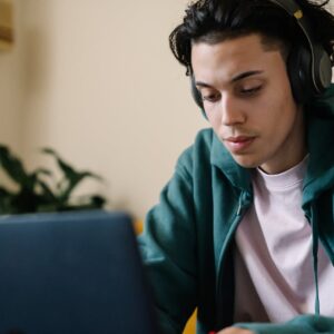 Focused young man studying indoors with headphones and laptop, perfect for education and technology content.